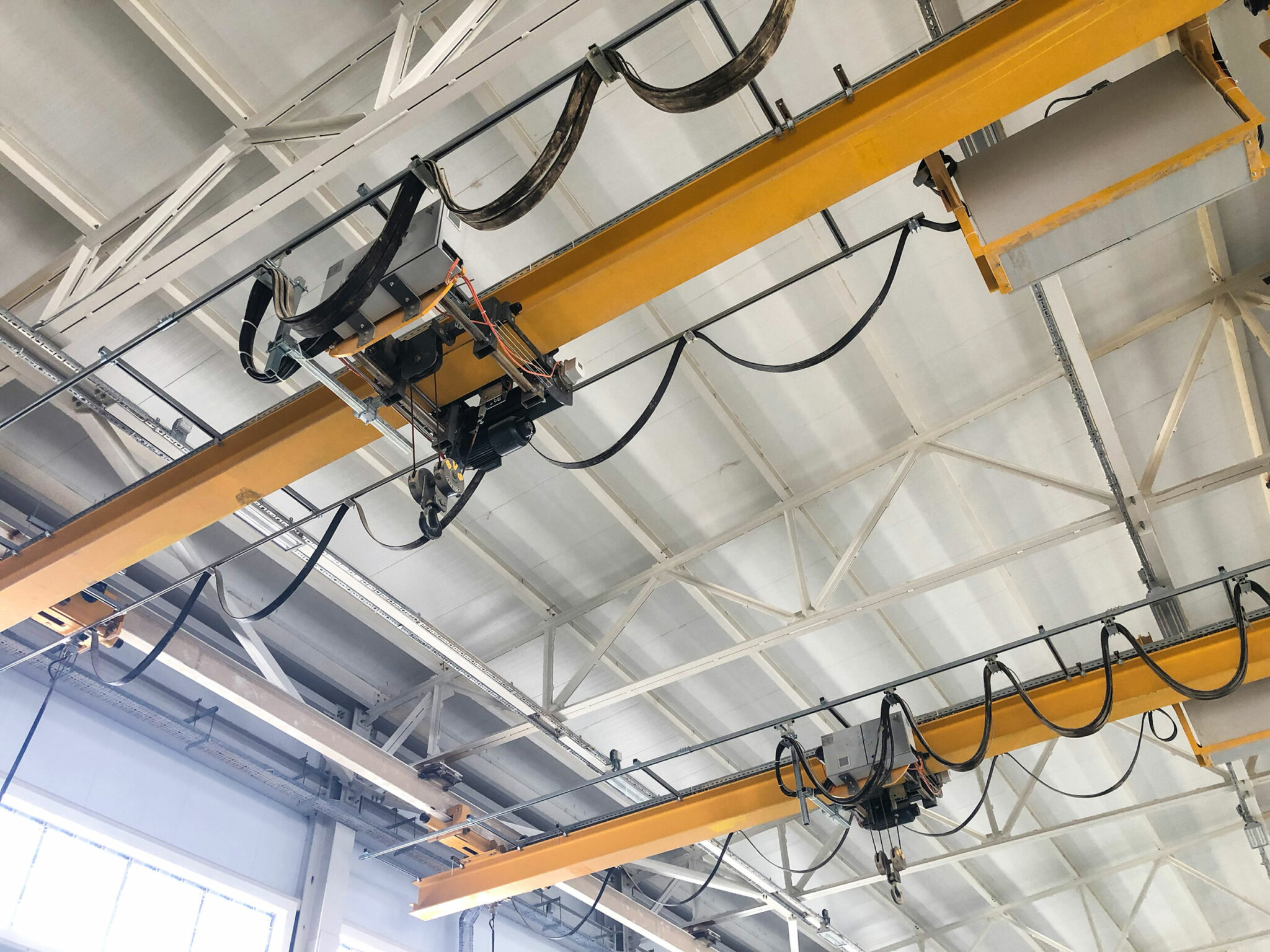 Eine Industriehalle mit Deckenlaufkränen: Zu sehen sind Träger, Hebevorrichtungen und Seile, die zum Transport von Lasten in der Produktion verwendet werden.