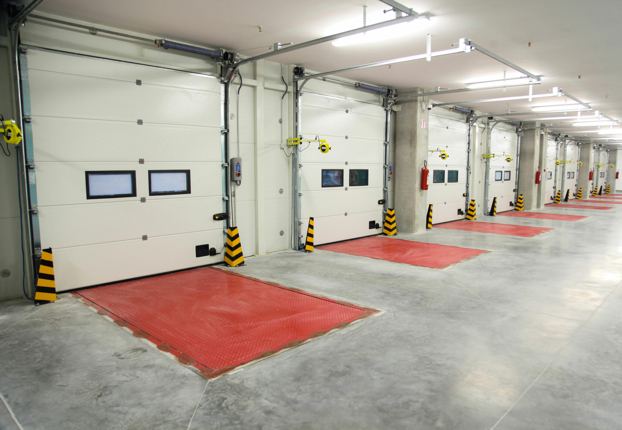Eine Reihe moderner Sektionaltore in einer Tiefgarage mit Automatik, Führungsschienen und Sicherheitszonen vor der Einfahrt.