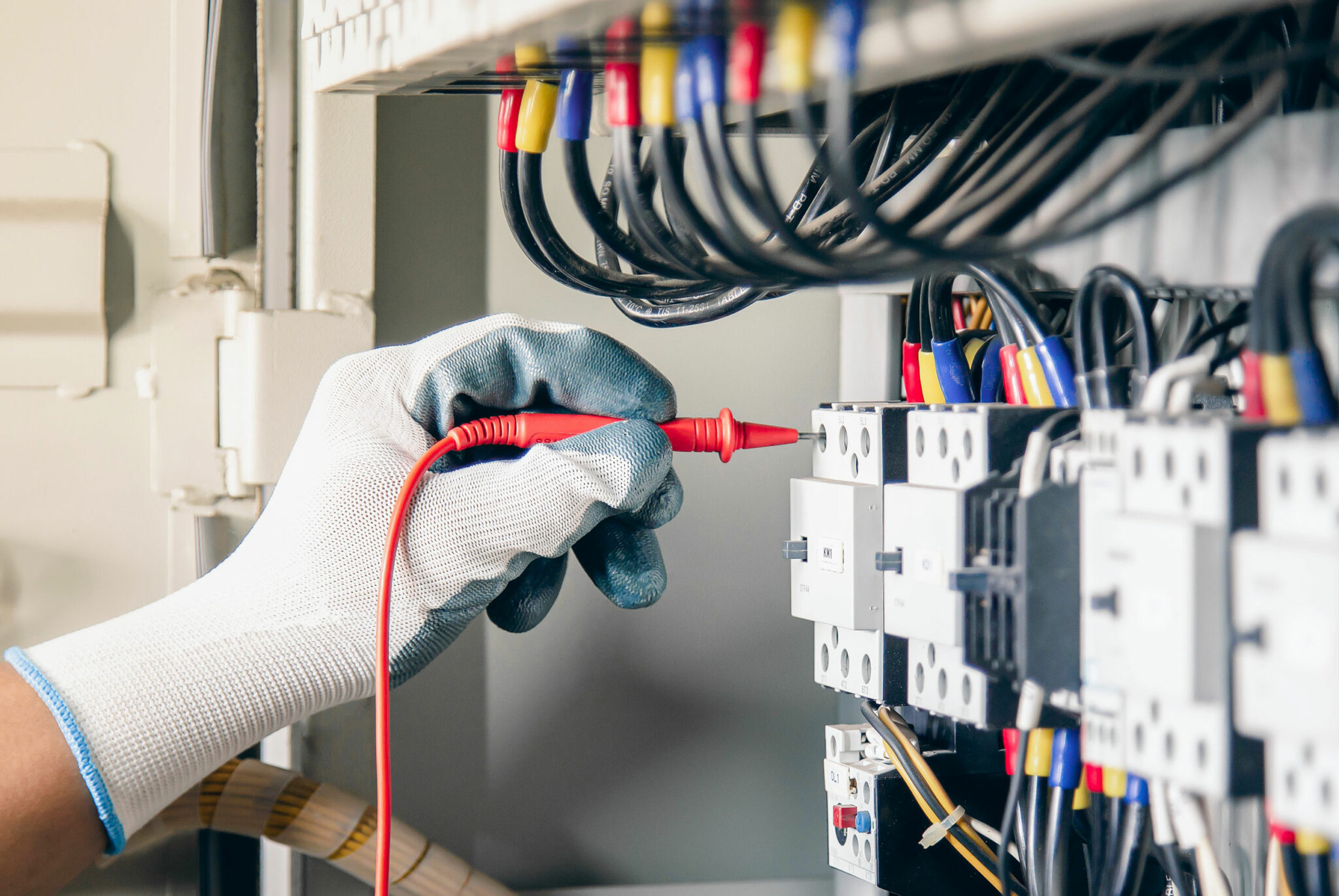Ein Fachmann, der Schutzhandschuhe trägt, überprüft die Schalttafel mit einer Messsonde, die an die Verkabelung und die automatischen Module angeschlossen ist.