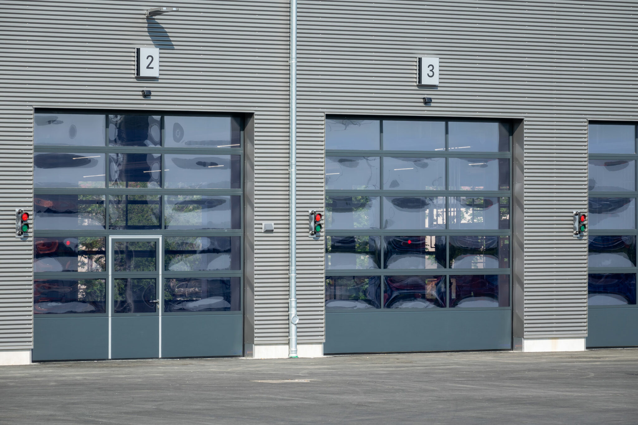 Die Fassade eines Industriegebäudes mit mehreren Sektionaltoren und Glaselementen; daneben sind Signalleuchten angebracht, die den Betrieb der Einfahrtssysteme anzeigen.