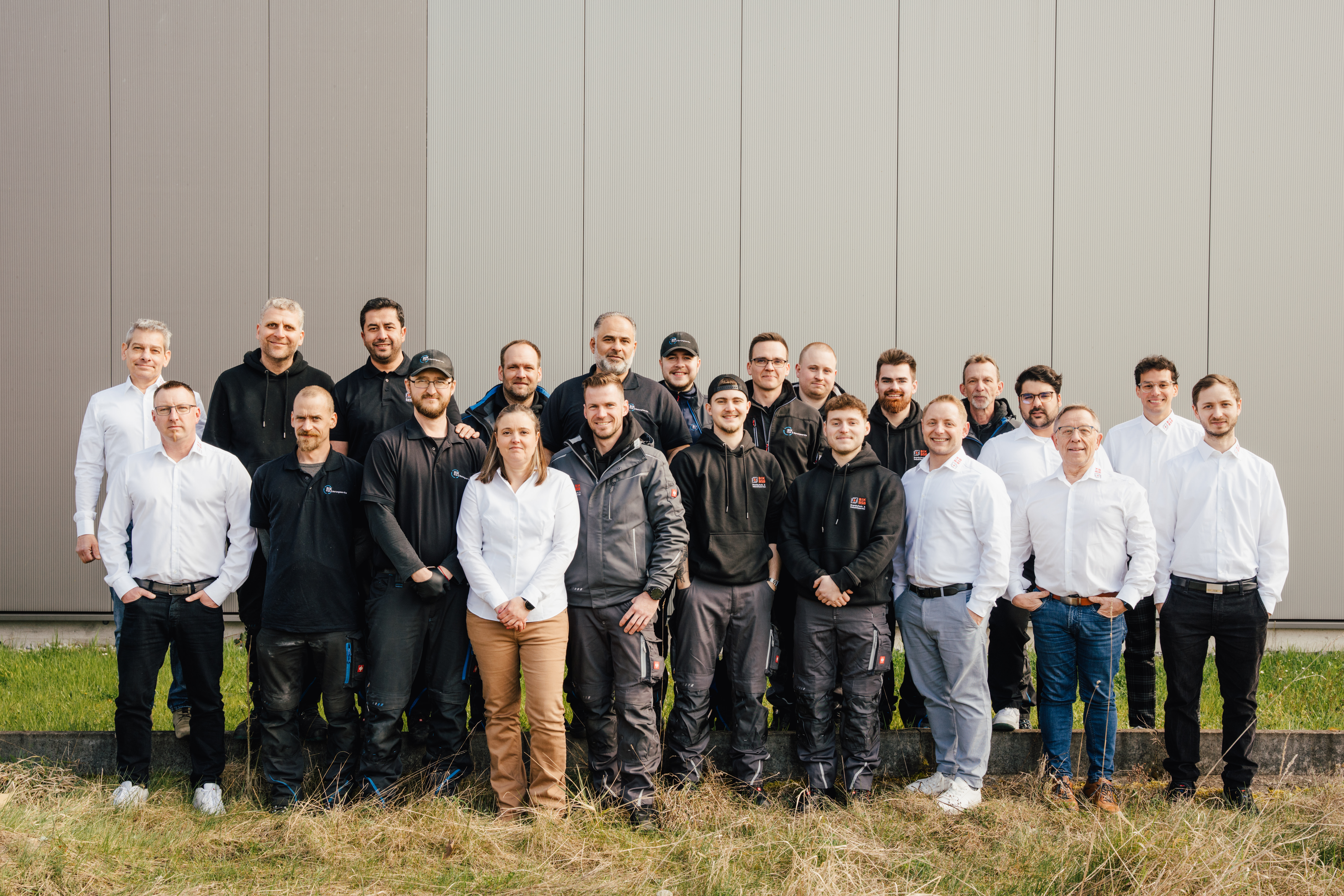 Eine Gruppe von Mitarbeitern der Firma BIK-BSB steht mit verschränkten Armen gemeinsam auf der Straße vor dem Gebäude und demonstriert damit Teamgeist und Professionalität.