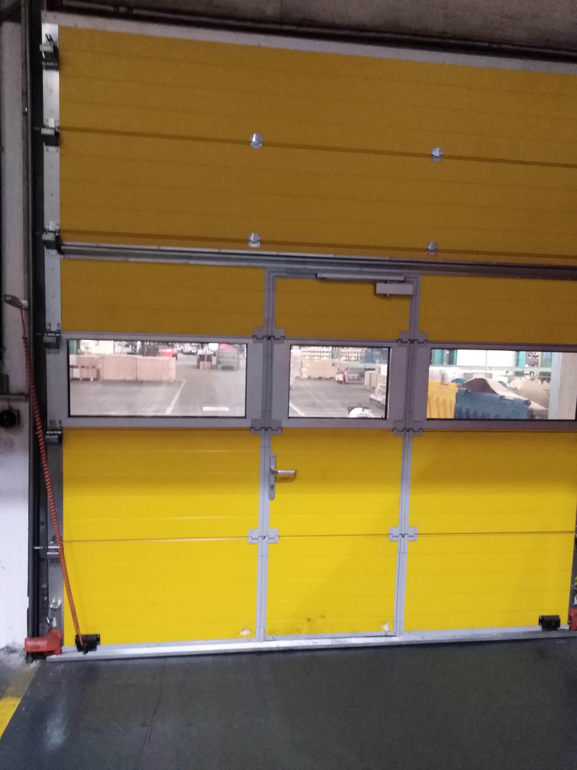 Das gelbe Sektionaltor mit integrierter Tür und Fenstern wurde in einer Industriehalle eingebaut und gewährleistet den Zugang sowie den Überblick über den Produktionsbereich.
